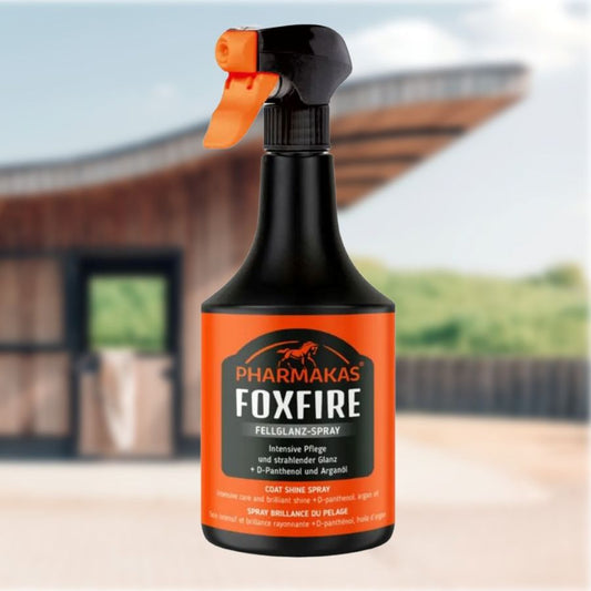Pharmakas Foxfire horse coat shine spray bottle with orange nozzle against a blurred outdoor background of stables