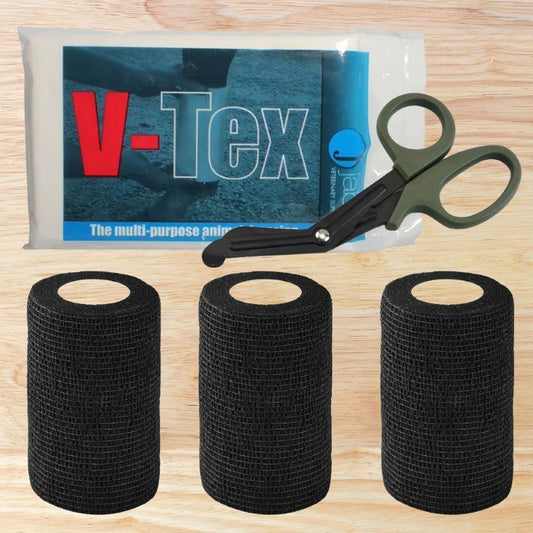 Three rolls of black cohesive bandage with a pair of first aid scissors and a V-Tex Animal Dressing Pack on a wooden surface.